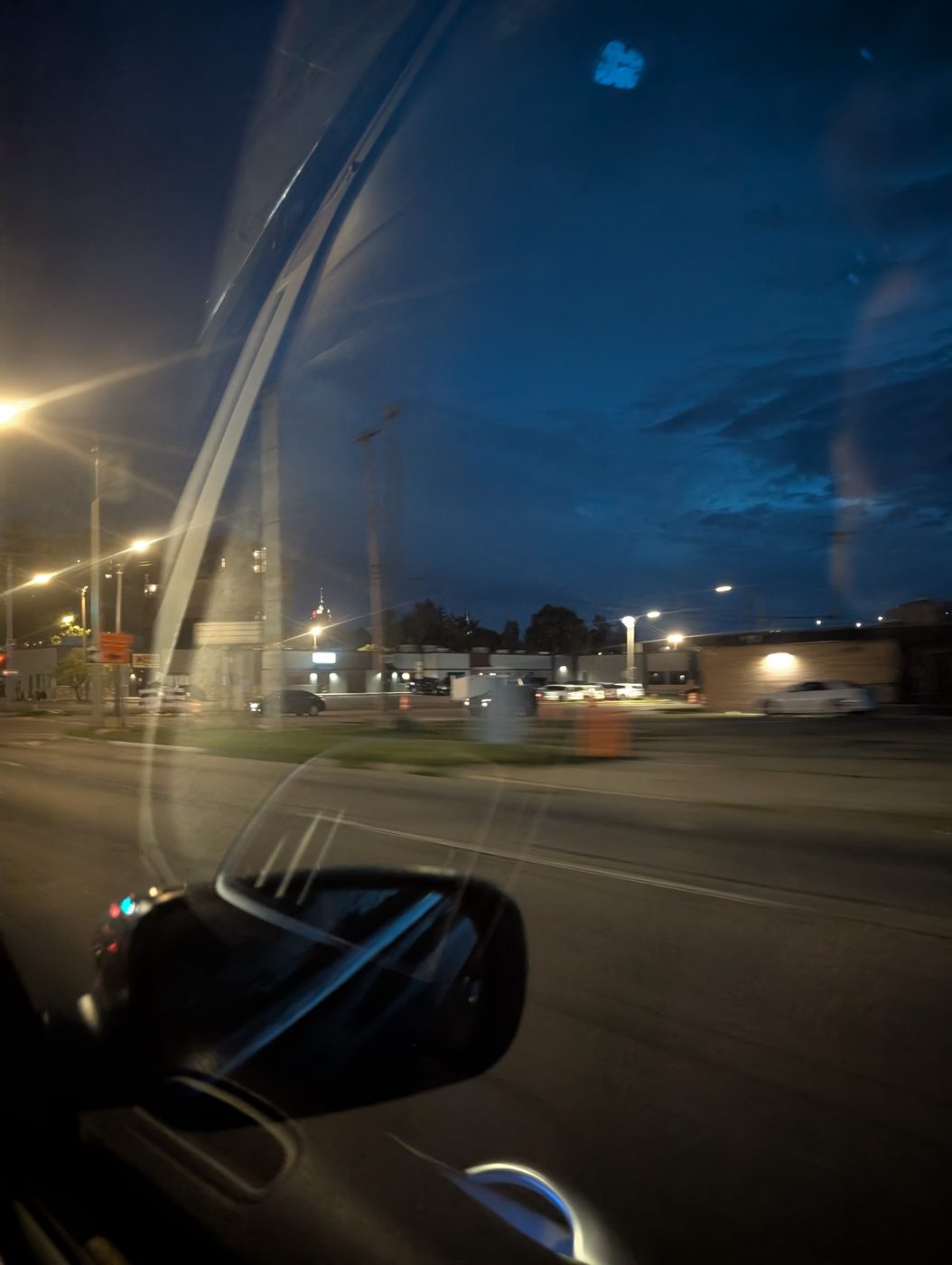 The 517 at the blue hour — deep cobalt twilight sky over streetlights and a commercial strip, seen past a car's side mirror