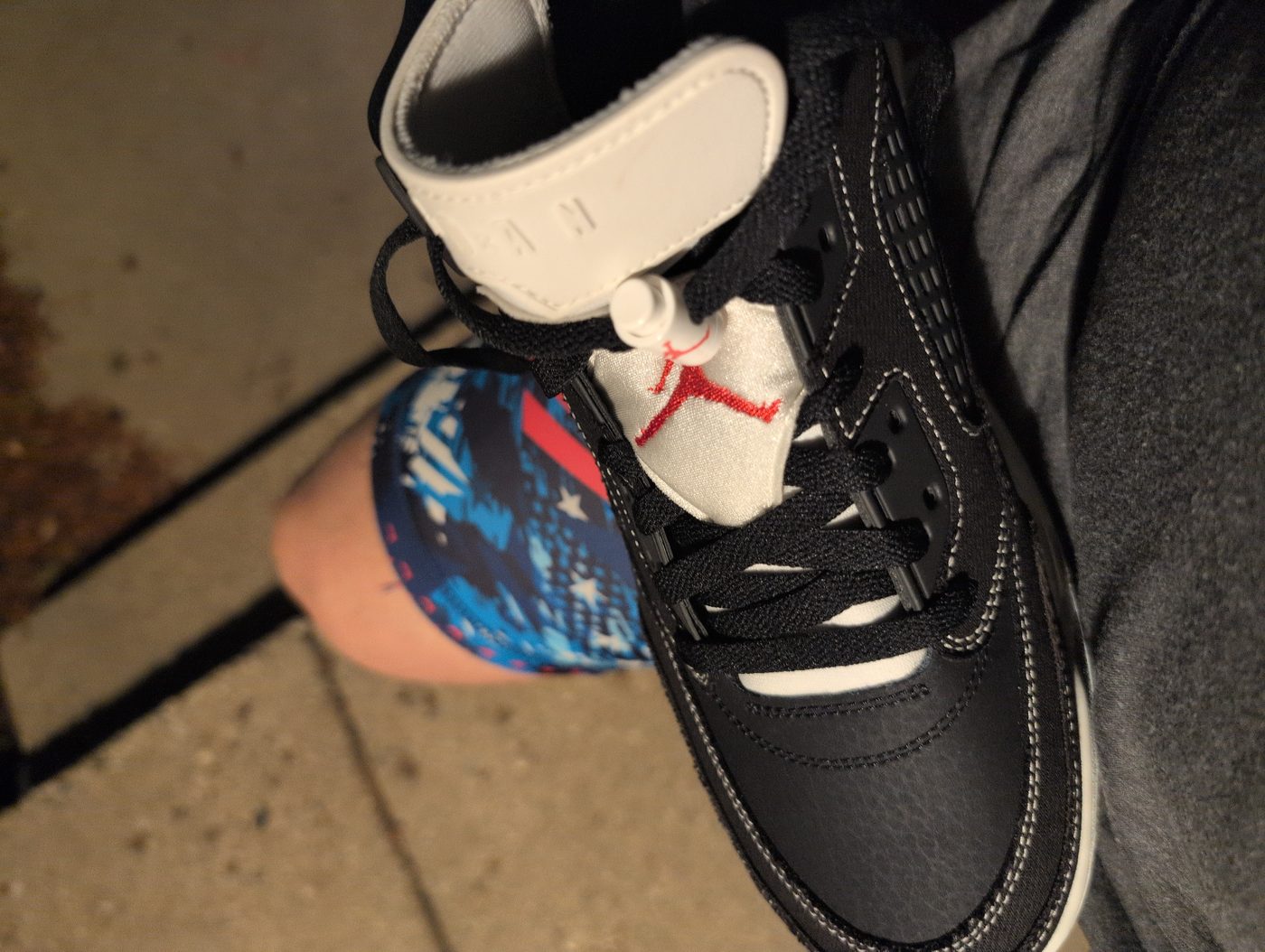 Black Air Jordans with a red Jumpman on the tongue, worn with stars-and-stripes socks, on a sidewalk at night